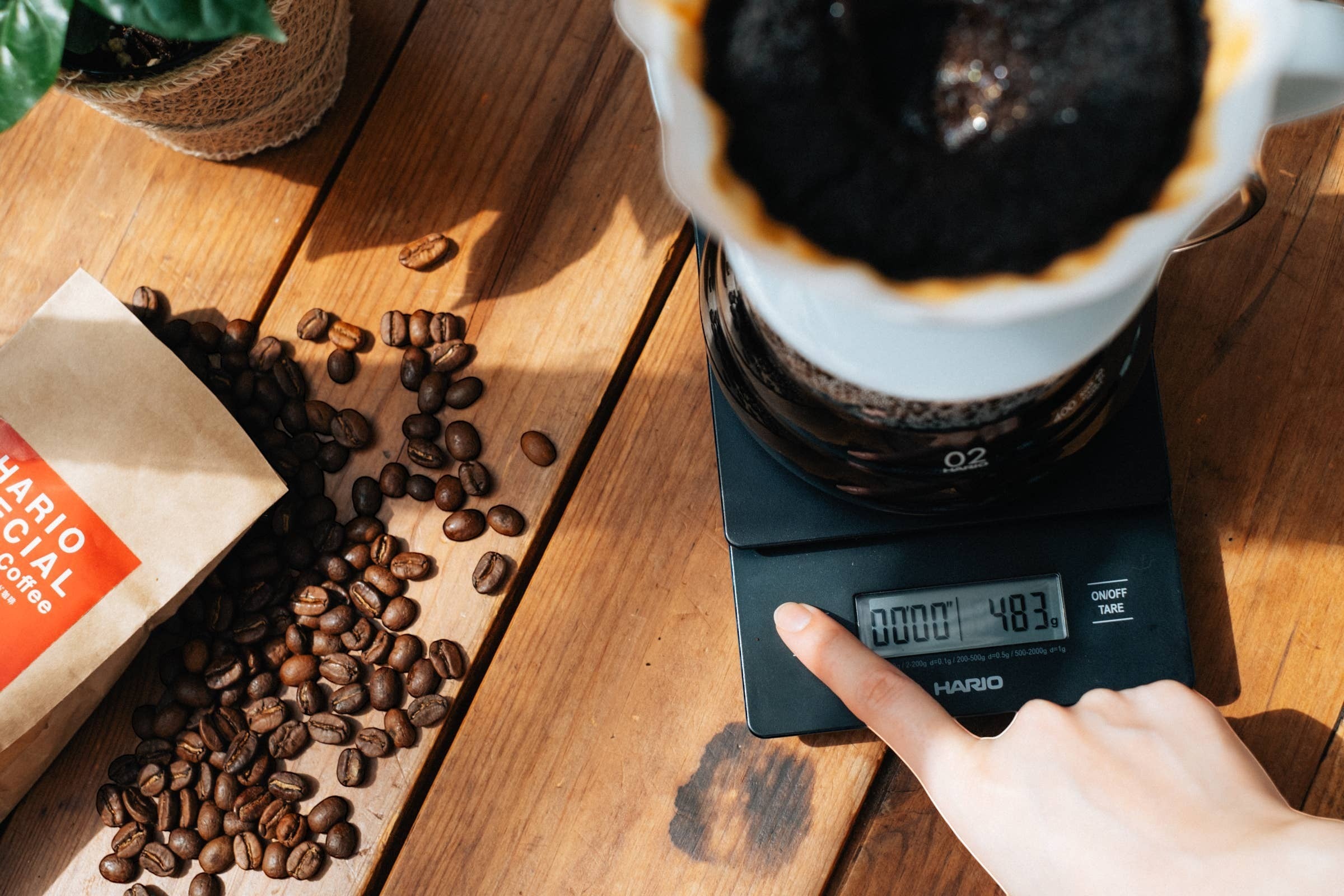 Báscula de café digital negra Nova Home Hario V60 con temporizador integrado sobre una mesa de madera con granos