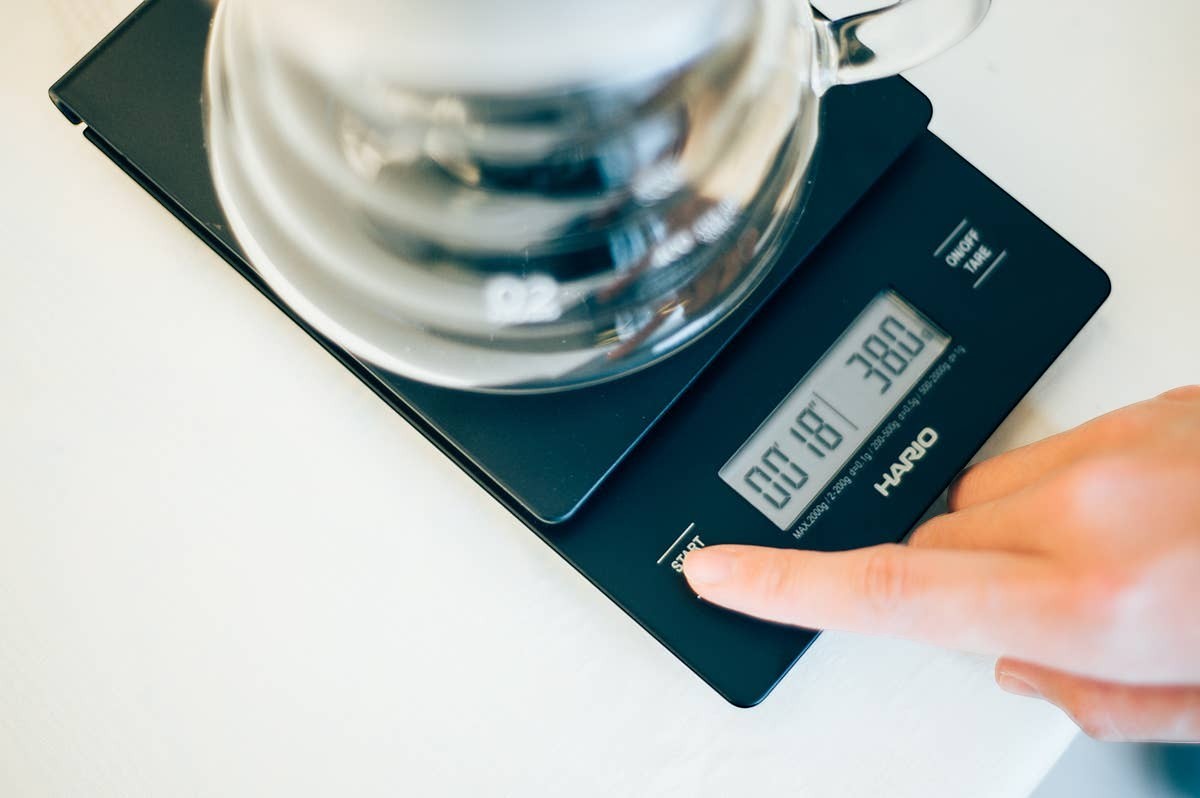Báscula digital negra Hario V60 con temporizador para café, mostrada en uso por Nova Home