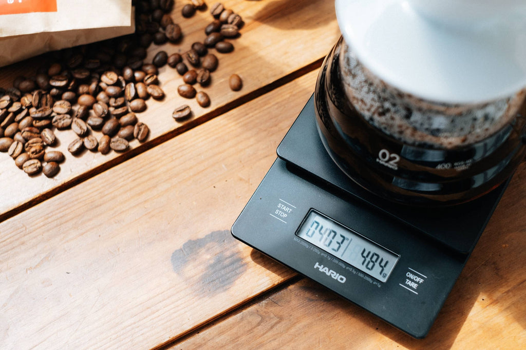 Báscula digital negra Nova Home Hario V60 con temporizador integrado para preparar café sobre una mesa de madera