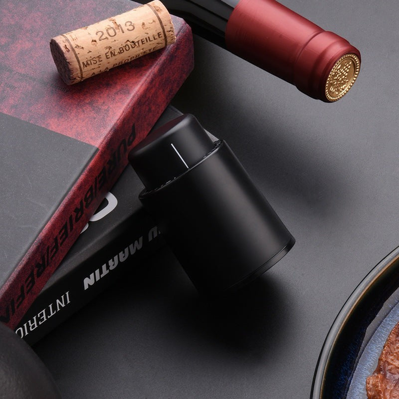 Tapón de vino negro Nova Home sobre mesa junto a una botella de vino y un corcho, accesorio de cocina elegante
